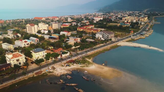 Lang co bay village and its surrounding natural landscape from above, featuring traditional fishing boats resting in the shallow lagoon, a coastal road, and lush green mountains meeting the sea