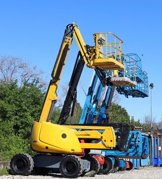 Group of cherry pickers lined up in a parking lot at the edge of the construciton site. Side view .