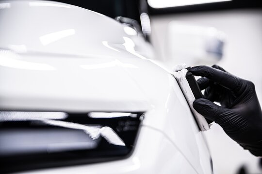 Close up of a professional detailer applying ceramic coating to a white car surface using an applicator. The process enhances gloss provides protection and creates a hydrophobic layer on the paint