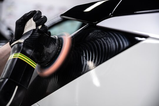 Close up of a detailer polishing a black car panel using a dual action machine. Visible polishing pattern shows the process of removing imperfections and restoring deep gloss and smooth finish