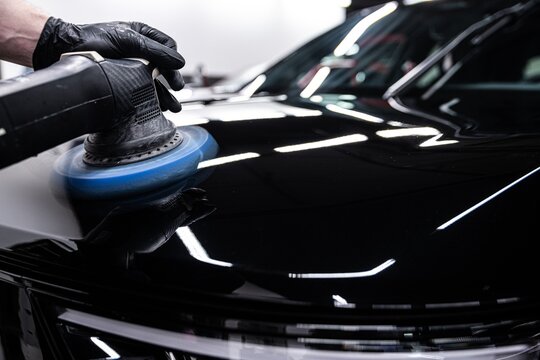 Close up of a professional detailer polishing black car paint using a machine buffer. The process enhances shine removes imperfections and creates a deep mirror like finish on the surface