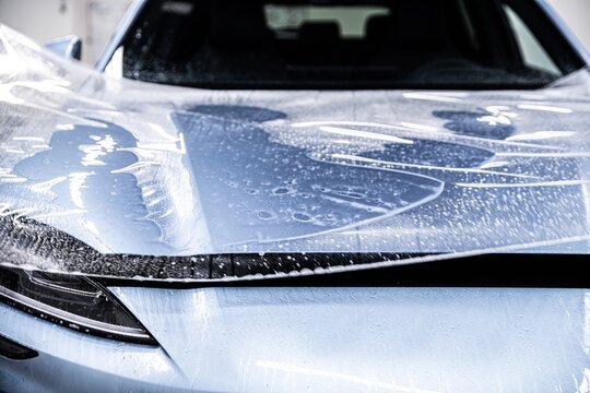 Close up of paint protection film being applied across the entire car hood. The film is carefully positioned and smoothed to ensure full coverage and long term protection
