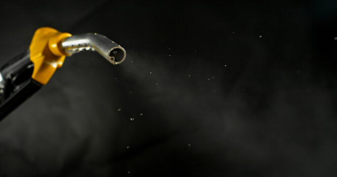 Gasoline droplets spraying from fuel nozzle on dark background, minimal остатky fuel flow. Concept of fuel shortage, depletion and energy crisis, dynamic motion, dramatic lighting.