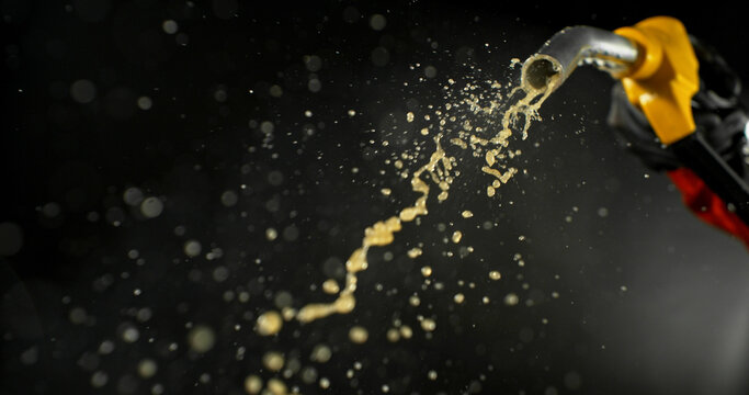Gasoline jet spraying from fuel nozzle held by hand on dark background. Dynamic liquid motion, refueling concept, energy supply, fuel usage, dramatic lighting, macro detail.