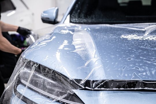 Close up of paint protection film being applied across the entire car hood. The film is carefully positioned and smoothed to ensure full coverage and long term protection