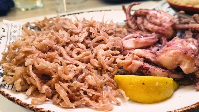 A plate of freshly fried elvers, young eels, served alongside crispy fried squid tentacles with lemon wedges in a seafood-specialized restaurant. Mediterranean seafood cuisine. High quality 4k footage