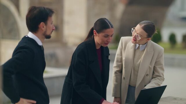 A group of business people collaborates on a laptop in an urban setting. They celebrate a successful outcome with high fives and enthusiastic cheers.
