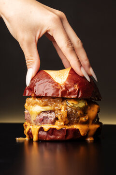 Close-up of hand grasping juicy cheeseburger in realistic style on dark backdrop, concept of rich comfort food