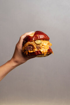 A hand holding a juicy cheeseburger with melted cheese in realistic style on a neutral background, concept of tasty fresh food