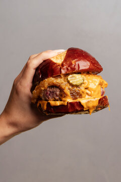 Hand holding a messy cheeseburger in clean photo style on grey background, presenting concept of indulgence