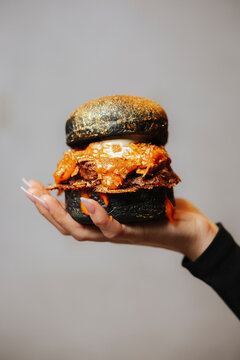 Black gourmet burger with gold toppings held in hand, in realistic style on soft background, concept of luxury street food