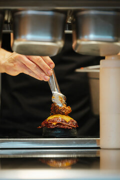 A close-up of a hand preparing a burger with cooked meat in a realistic style on a kitchen background, concept of gourmet cooking