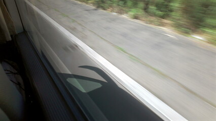 Motion blur view from bus window showing fast-moving asphalt road with faint shadow of bus and dry vegetation along roadside © Marco