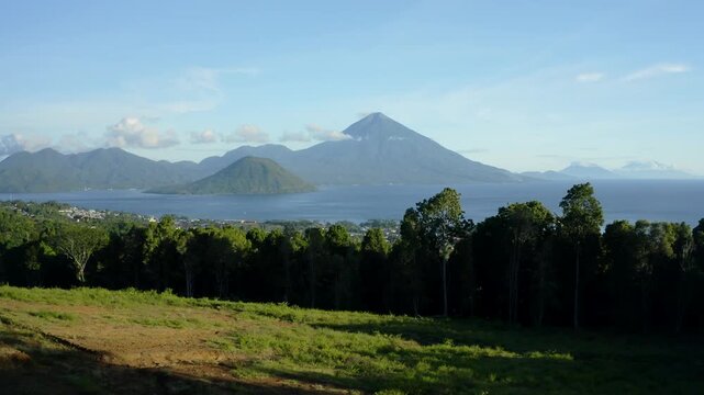 Aerial view of majestic volcanic peaks rising above the sea with lush tropical forests and a clear blue sky Ternate, North Maluku, Indonesia.