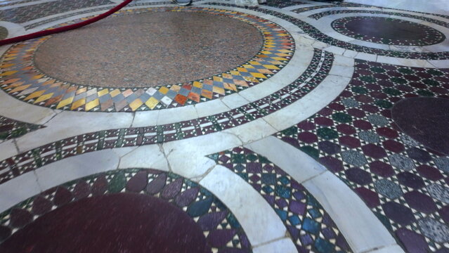 Circular marble mosaic floor inside Basilica di Santa Prassede in Rome with geometric patterns, Latin inscription, and visitors walking across historic design