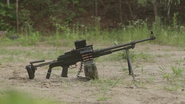 Loaded PKM machine gun on tripod resting on sandy ground.