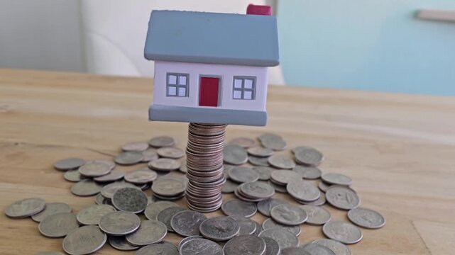 House model stands on stack of coins with other coins spread around the table
