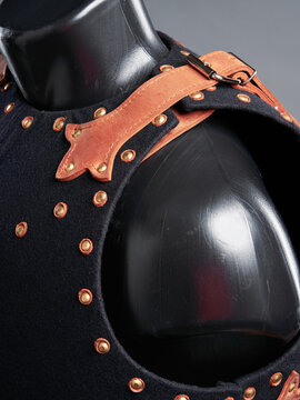 Close-up of black felt armor with brass rivets and decorative tan leather strap worn on a mannequin shoulder for medieval costume use.