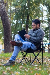 Fototapeta premium A latino man on vacation sitting in nature reading a book