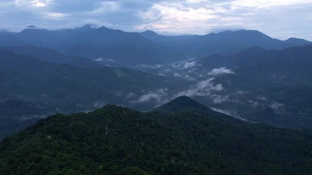 Fog moving across layered green hills and valleys in Kerala, tropical rainforest landscape from aerial view.