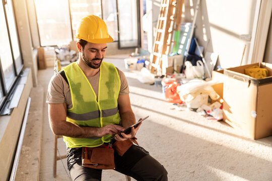 Construction worker uses a tablet while sitting in a work area during daylight hours on a job site