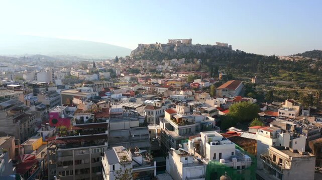 Aerial drone view of Athens city at sunset with warm light over rooftops and Acropolis hill in the background, Greece urban cityscape.