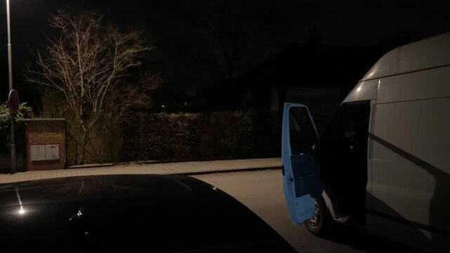Night delivery van parked with open door on suburban street, lamppost casting shadow, quiet residential curbside scene, cargo bay silhouette and calm evening atmosphere
