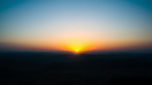 Golden rays of dawn breaking over the horizon into a deep blue pre-dawn sky.