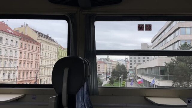 Train window cityscape colorful facades passing, empty seat in foreground, overcast sky, closeup of apartment blocks, slow suburban transit mood, subtle reflections on glass