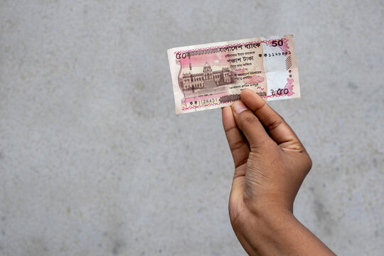 A person is holding a Bangladeshi fifty Taka banknote against a plain wall background. This visual is ideal for South Asian financial news, banking services, and economic growth stories.