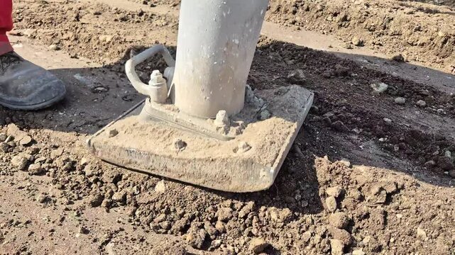 Close-up diagonal front view of a jumping jack rammer compacting soil on a construction site.