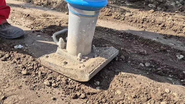 Slow motion close-up of a vibrating rammer hitting the ground and compacting loose soil.