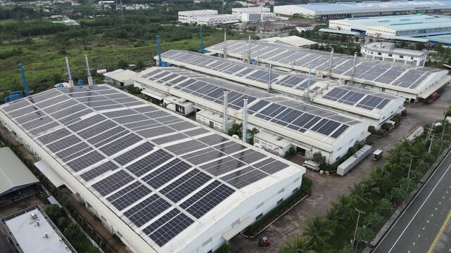 Aerial view of extensive solar panel installations on the roofs of industrial buildings and factories surrounded by greenery in An Phuoc, Dong Nai, Vietnam.