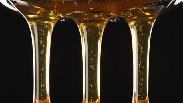 Close up golden honey dripping from a glass vessel with shiny textured background in high detail