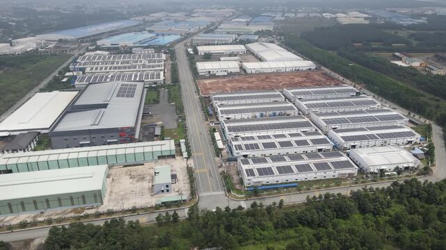 Aerial view of large industrial warehouses and manufacturing plants with solar panels on rooftops along a central road in An Phuoc, Dong Nai, Vietnam.