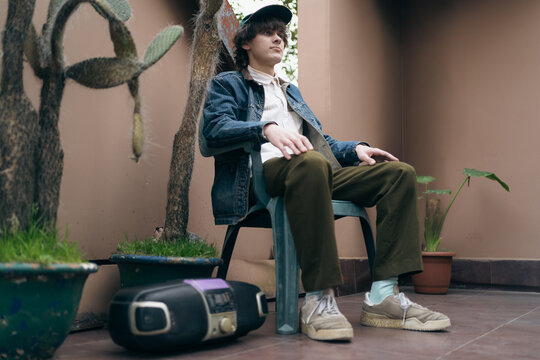90s fashion young man seated with portable stereo, denim jacket and relaxed pose, blending vintage menswear, analog music culture, retro lifestyle and nostalgia.