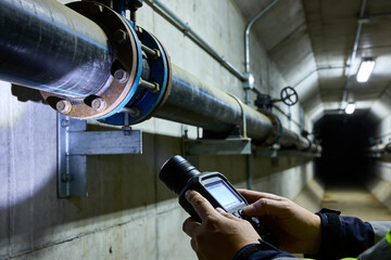 Technician inspecting large industrial pipes with a handheld device in a tunnel © Snide12