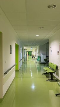 Bright green hospital corridor in daytime, polished reflective floor, row of lime waiting chairs, accessible handrails and ceiling panels, medical trolley near distant doorway,