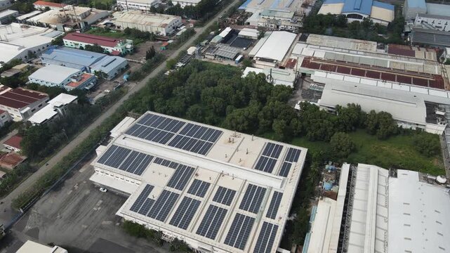 Aerial view of solar panels installed on an industrial building roof surrounded by lush green trees and other warehouses in An Phuoc, Dong Nai, Vietnam.
