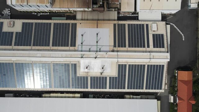 Aerial view of solar panels on an industrial warehouse roof with a small red-roofed building and surrounding greenery in An Phuoc, Dong Nai, Vietnam.