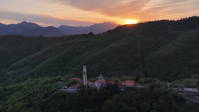 Aerial view of Passo Di Cento Croci church and bell tower nestled in the forested hills of Liguria at sunset Varese Ligure, Liguria, Italy.