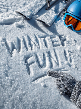 words WINTER FUN Written in the soft snow with a snow glove, the fronts of two skis and a Helmet and goggles