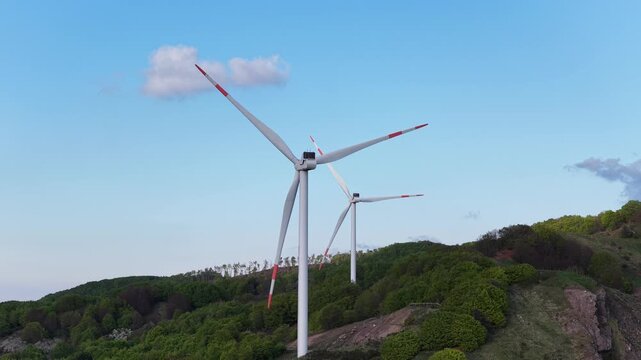 Aerial view of wind turbines at Passo Di Cento Croci on green hills under a blue sky in Varese Ligure, Liguria, Italy.