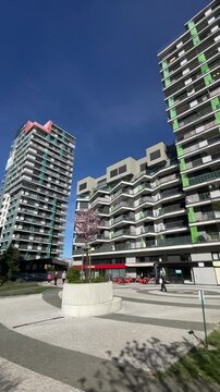 Modern apartment tower vertical stock video showcasing sunny courtyard and landscaped plaza, groundup vertical shot reveals green accent strips, pink roofline, rows of balconies,