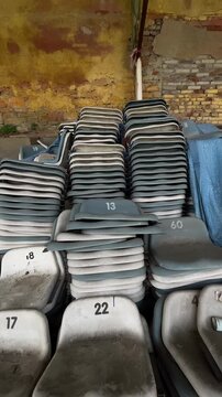 Vertical stock video stacked numbered seats dusty warehouse setting with weathered plastic seating piled against peeling yellow brick wall closeup vertical pan shows numbers and,