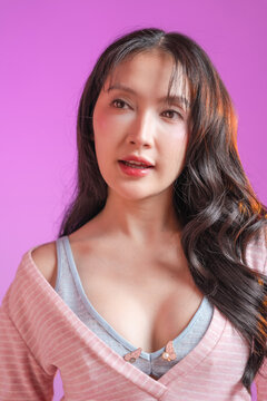 beautiful young East Asian woman with long wavy dark hair and a bright toothy smile, looking away and laughing. She is wearing a soft pink striped top with a light blue inner layer, set against a vibr