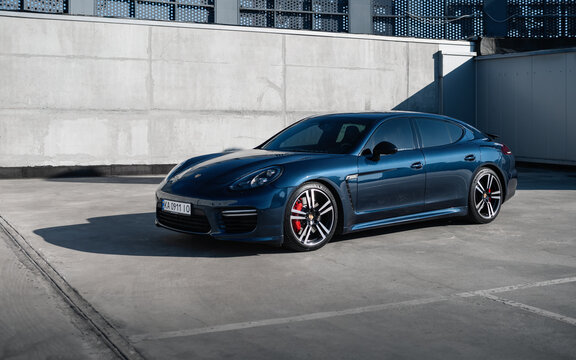 blue Porsche Panamera in front of concrete wall on sunny day. Three quarter front view of german grand tourer in rooftop parking lot. Kyiv, Ukraine - April 04 2026