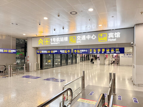 Modern Chinese airport terminal interior with bilingual directional signage in Chinese and English showing directions to Terminal 1, GTC transportation center, and hotel. Clean, spacious departure hal
