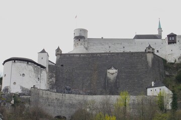 Detailed view of massive medieval stone walls of Hohensalzburg Fortress with historic sculpted coat of arms relief ancient round tower and majestic fortification bastions on Monchsberg hill. © Koapan