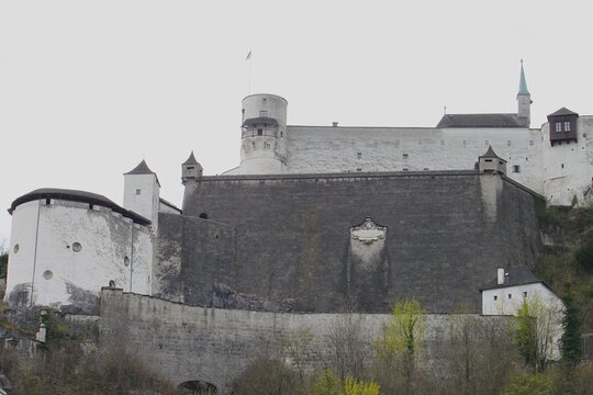 Detailed view of massive medieval stone walls of Hohensalzburg Fortress with historic sculpted coat of arms relief ancient round tower and majestic fortification bastions on Monchsberg hill.